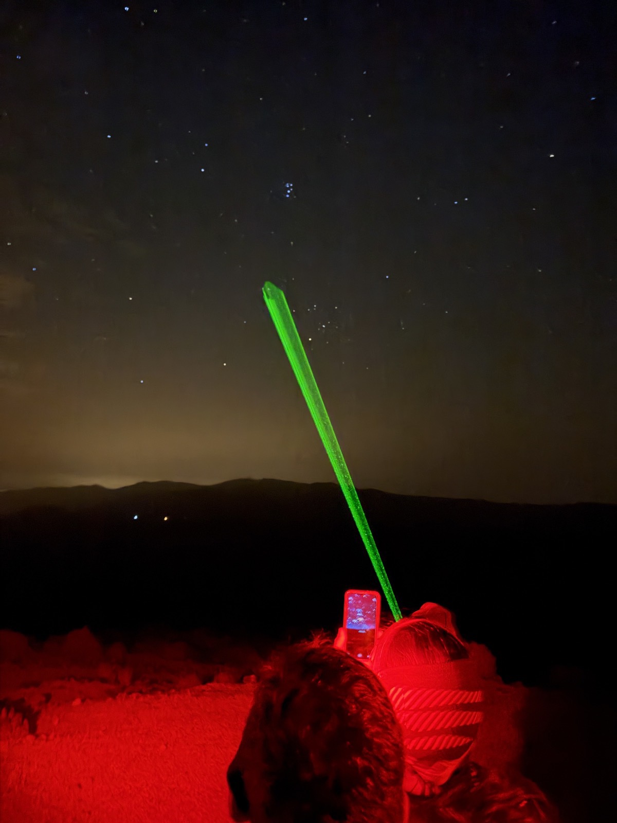 Green laser pointer aimed at a star-filled sky during a night stargazing session on Mount Teide, the group lit red by head torches